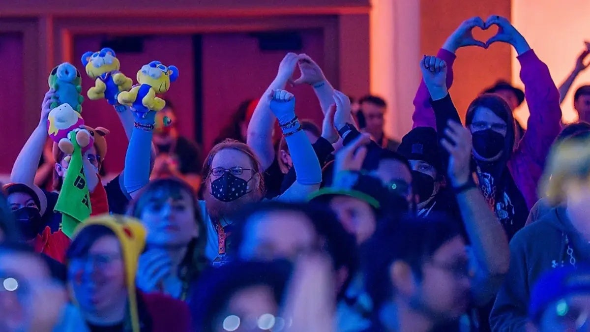 Three people make hearts with their hands in the crowd at Games Done Quick