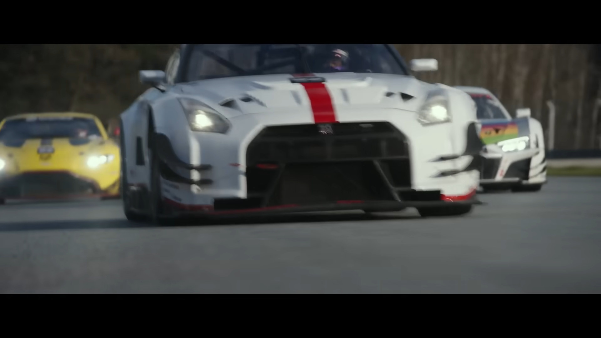 Gran Turismo movie trailer screenshot showing Jann&rsquo;s white car in front of two others on the track, facing towards the cars from low down as they drive towards the camera
