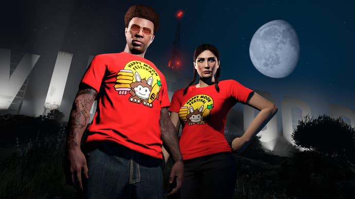 Two GTA Online characters in seasonal red t-shirts standing in front of GTA V’s Vinewood sign at night.