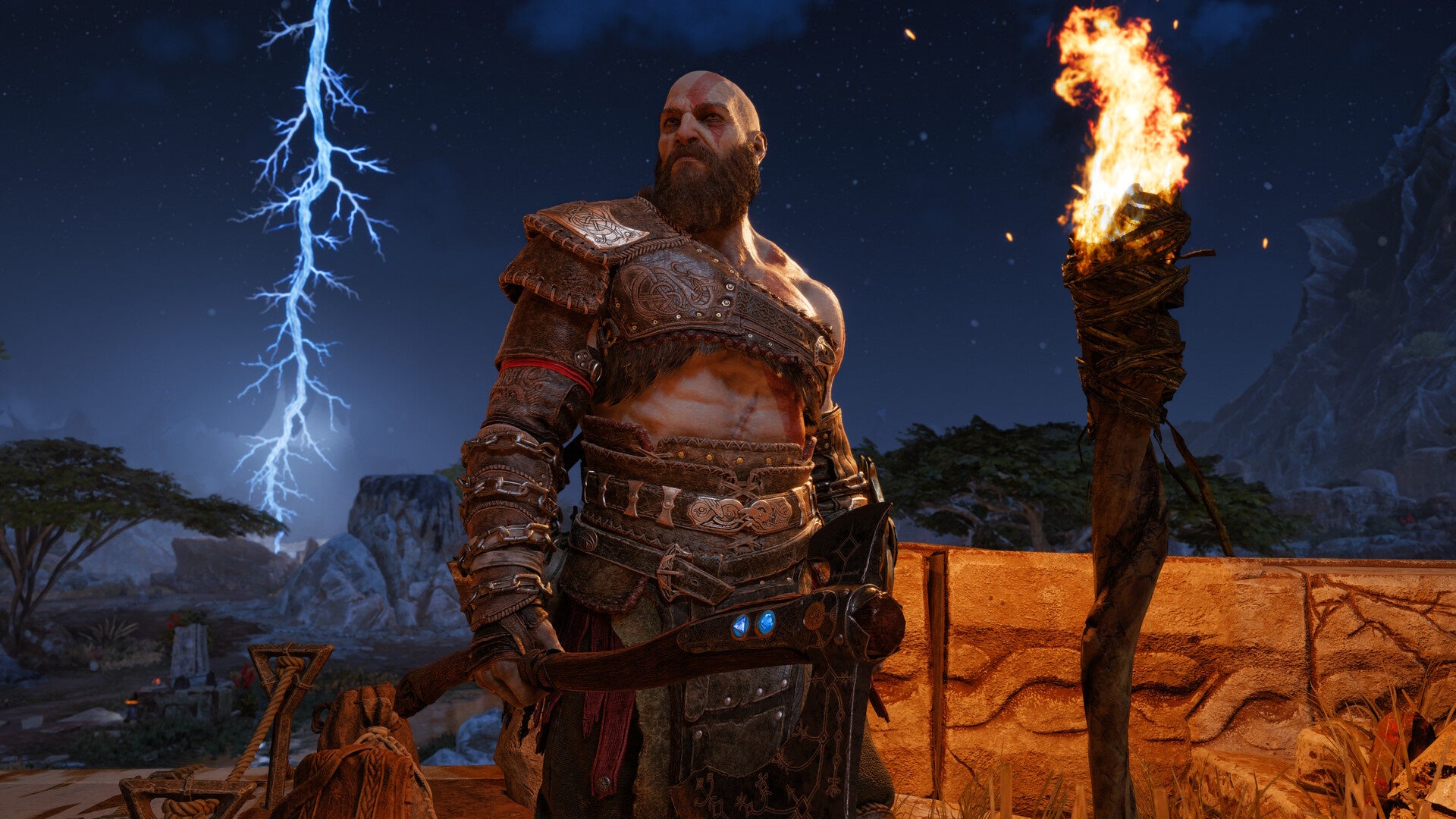 Kratos in God of War Ragnarok looking off the the left in front of a night sky with lightning in the background.