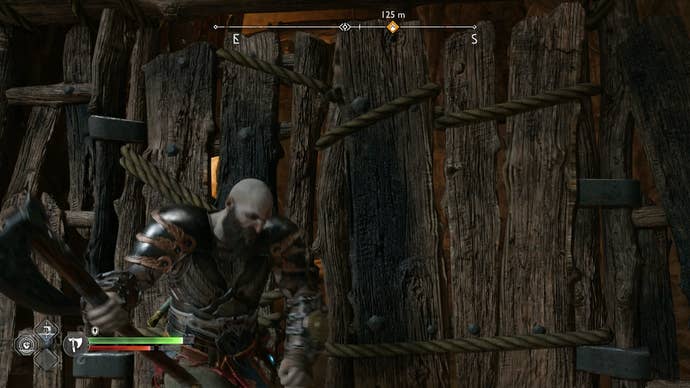 Kratos using his axe to destroy a wooden barrier in The Applecore in God of War Ragnarok