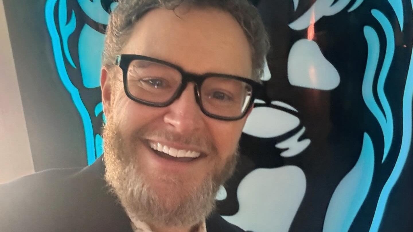 Gordy Haab smiles in front of an image of the BAFTA logo
