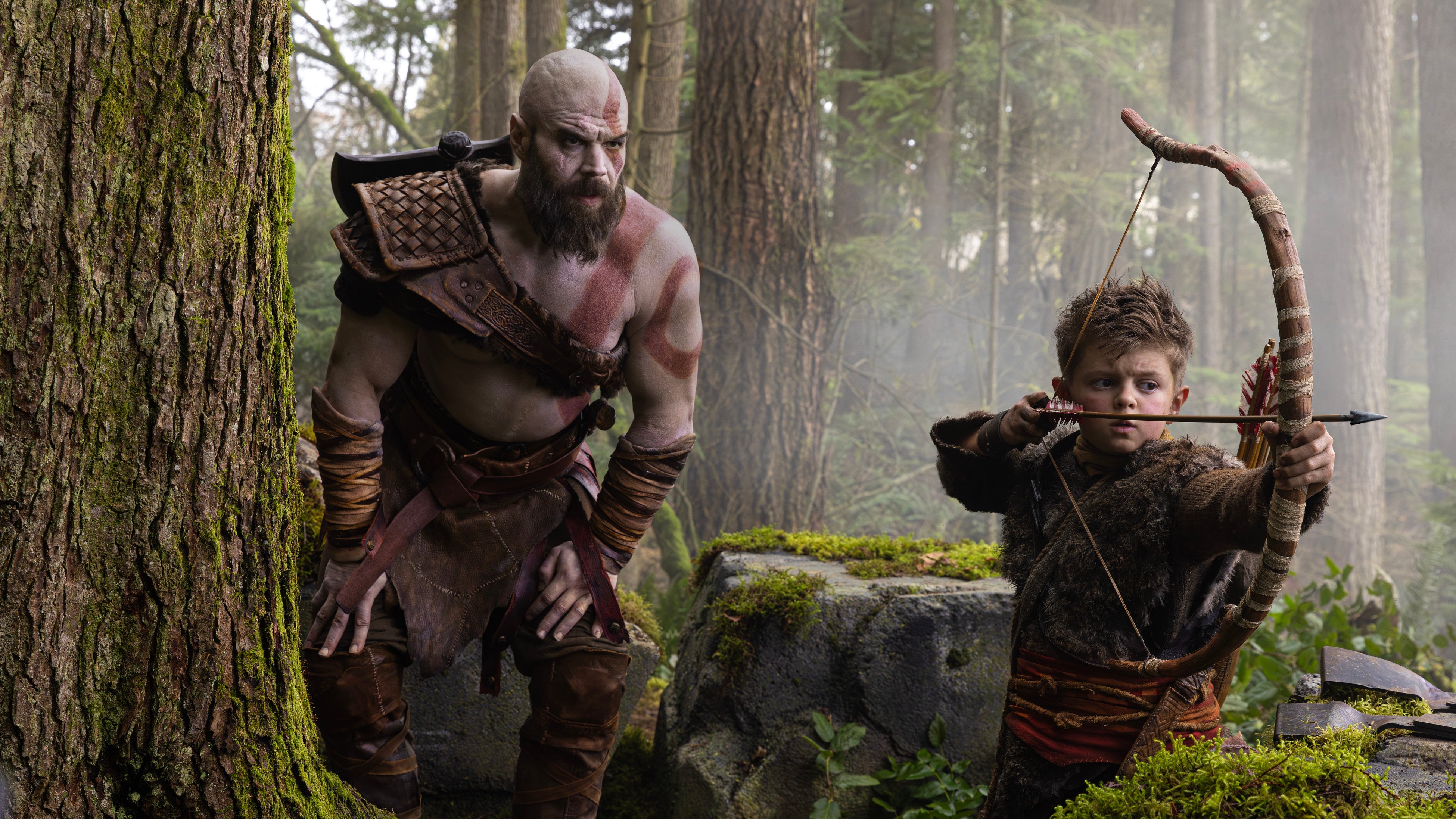 A still from the God of War TV series showing Kratos teaching Atreus, a young boy, how to hunt.