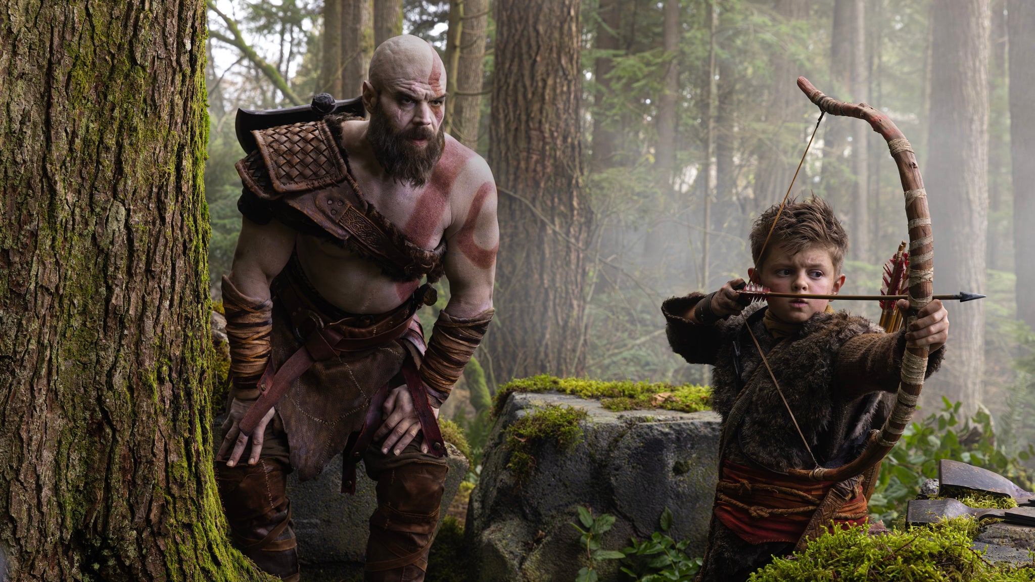 A still from the God of War TV series showing Kratos teaching Atreus, a young boy, how to hunt.