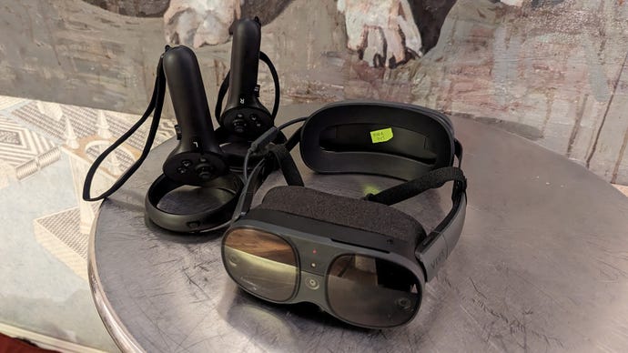 The Vive XR Elite virtual reality headset on a table, next to its two wireless controllers.