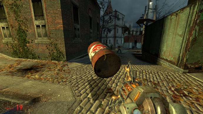 The player holds an explosive barrel in mid-air using the gravity gun in Half-Life 2
