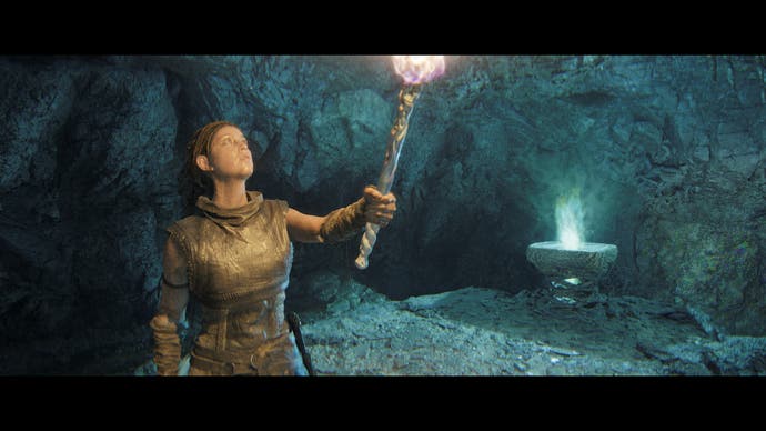 Hellblade 2 screenshot showing Senua holding a torch up in a small cave