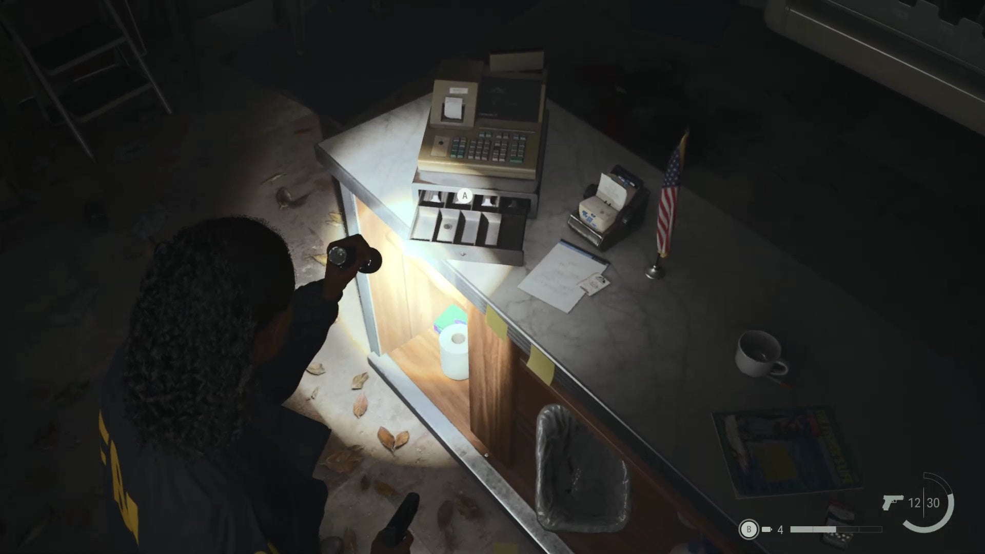 sage shining her flashlight on a cash register on top of a messy counter in a rundown general store