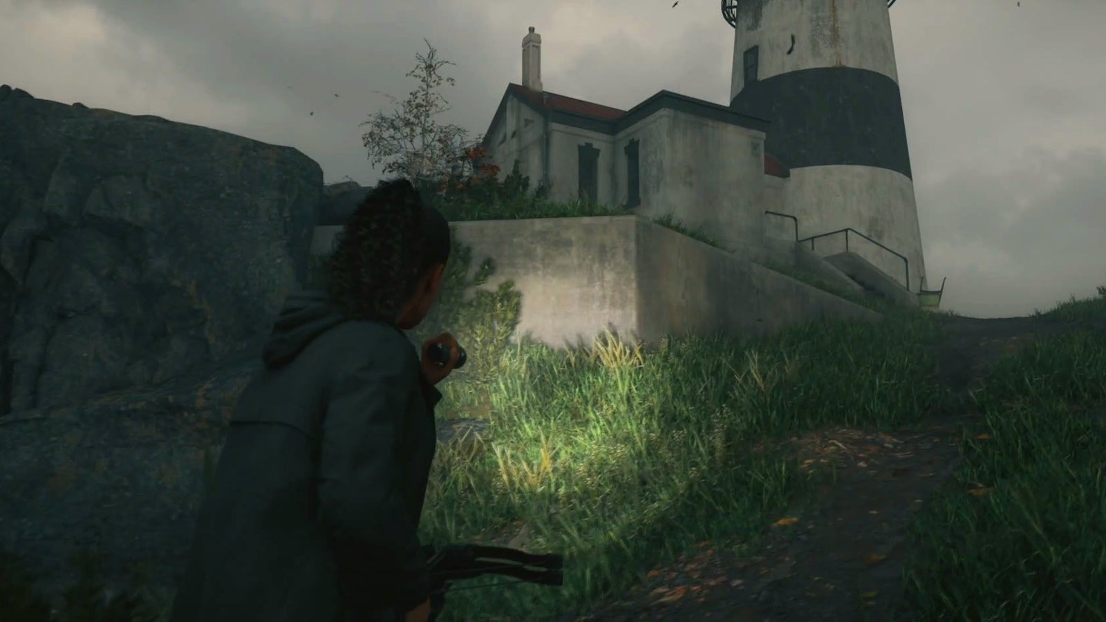 saga aiming her flashlight at a lighthouse on the edge of a cliff with a muddy path below it