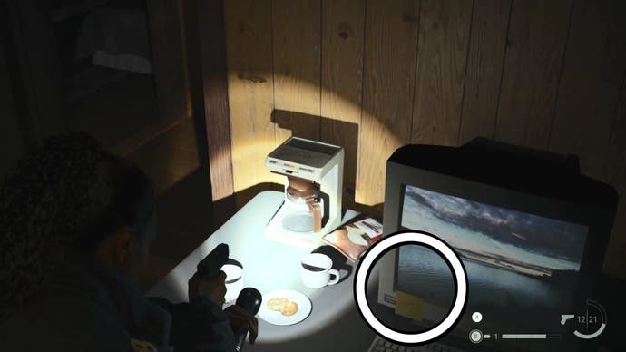 saga shining her flashlight on a coffee percolator beside a computer monitor, with a white circle  around a post it note stuck to the monitor