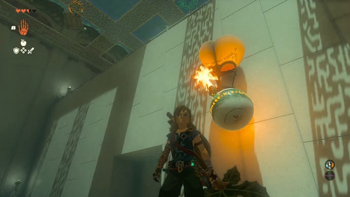 Link standing in the Sinakawak Shrine, as a hot air balloon with a metal ball attached to it floats higher into the air.
