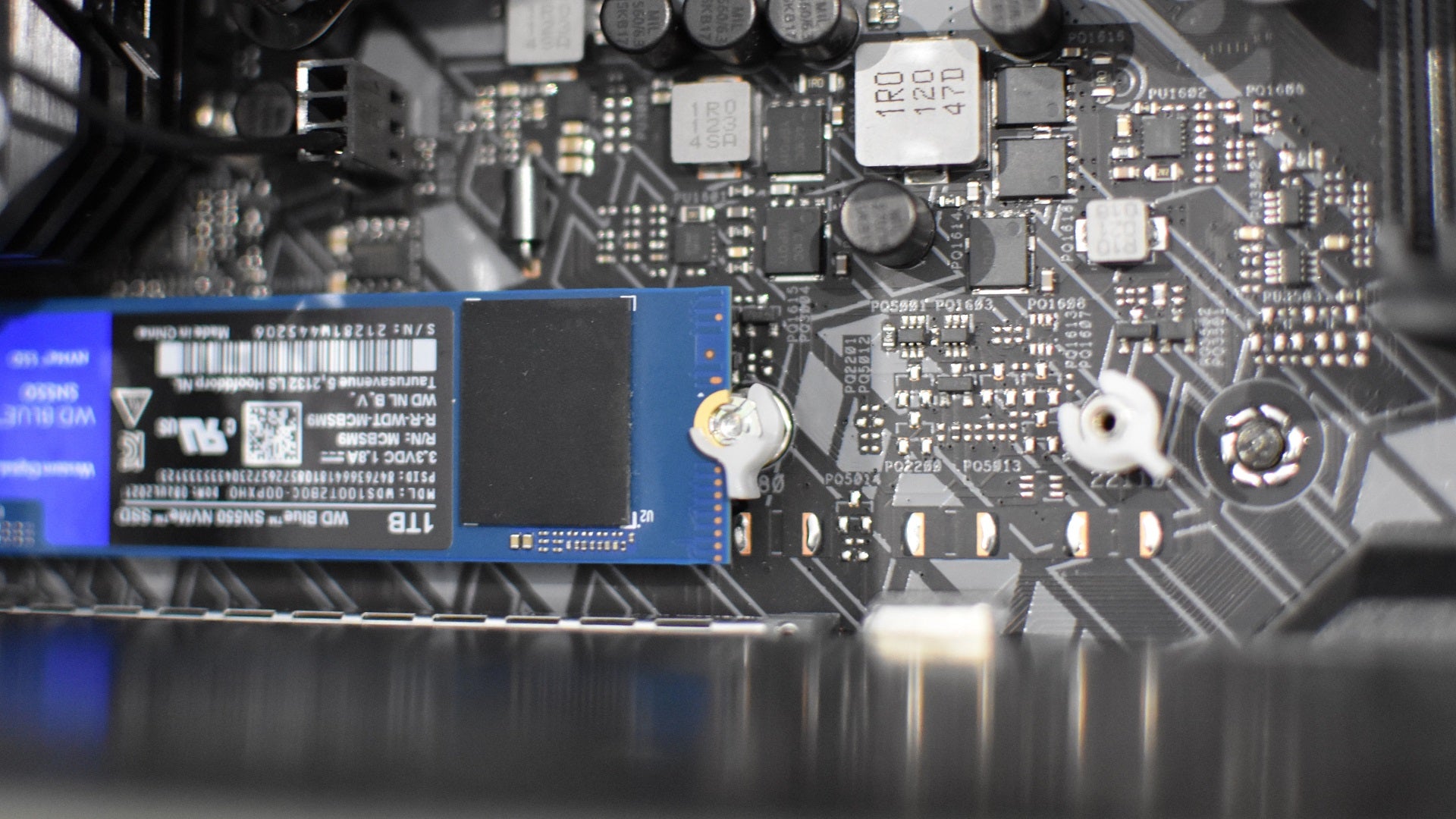 Step 3 of how to install an NVMe SSD: Secure the SSD in place by pressing it down flat and either tightening the small screw at the opposite end, or rotating the small plastc clip over it.