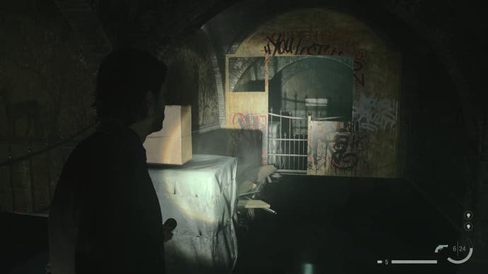 Alan pointing a flashlight at a dilapidated wall covered in graffiti with a gap in it, in a dark rundown train station tunnel