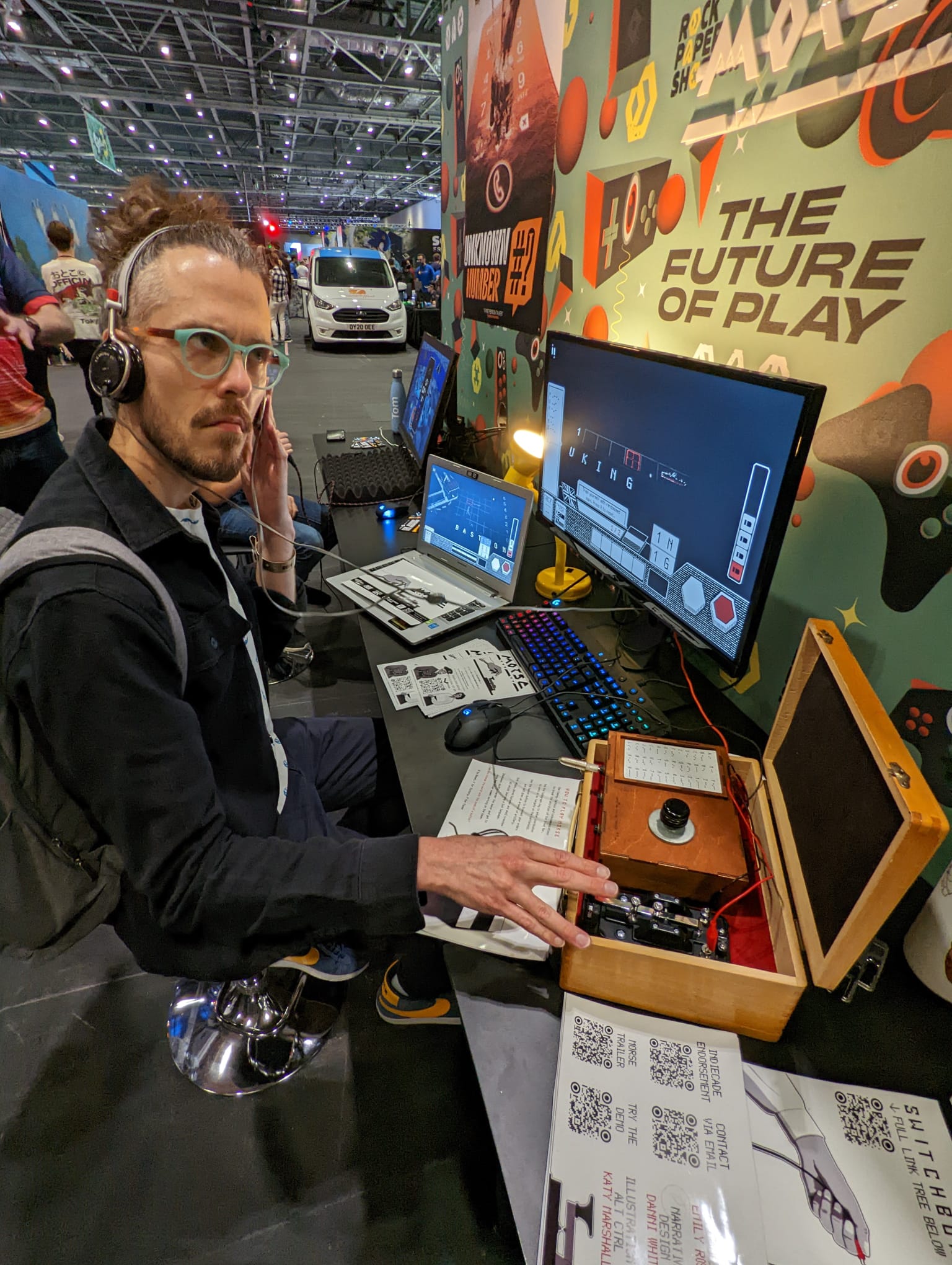 Bertie playing a Morse Code game at EGX. There&rsquo;s a wooden box on a bench with the familiar little Morse Code clicker on it, and a big launcher button nearby. Bertie looks rapt.
