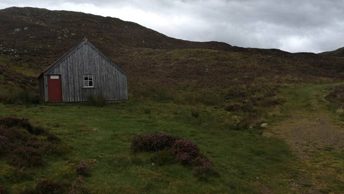 A photograph of a wooden hut with a red door on a moor in Scotland