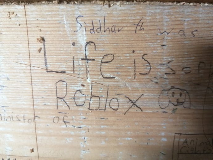 The scrawled message "Life is Roblox" on a wooden wall