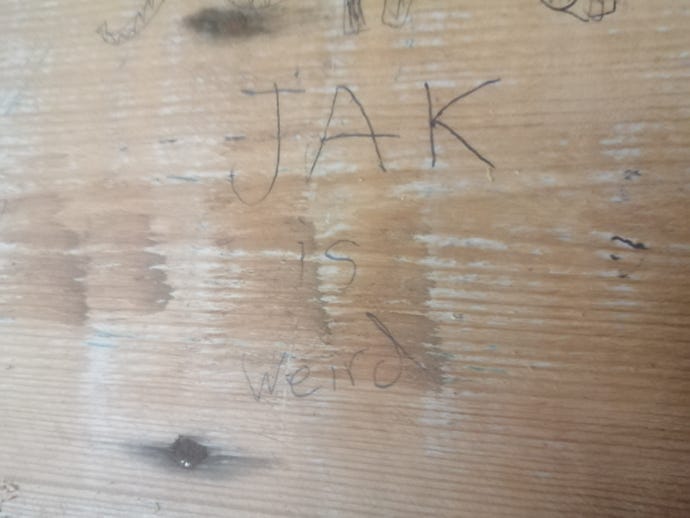The words "Jack is weird" scribbled on a wooden wall