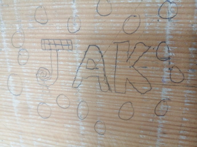 The word "Jak" written in cartoon font on a wooden wall in biro