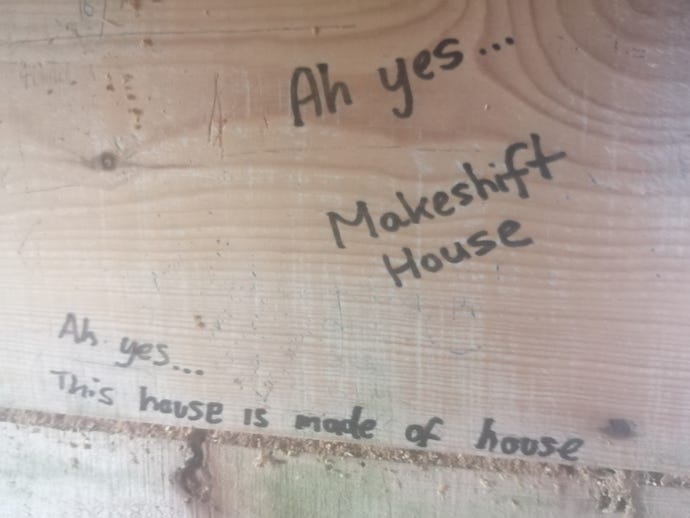 The phrases "Ah yes... makeshift house" and "Ah yes... this house is made of house" written in felt tip on a wooden wall