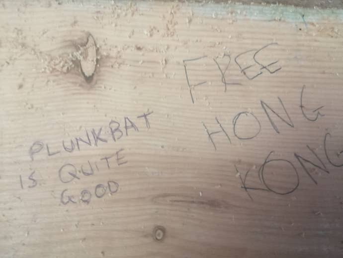 The phrase “Plunkbat is quite good”, written by the person taking the photo, next to the phrase “FREE HONG KONG”, written by somebody else, on a wooden wall