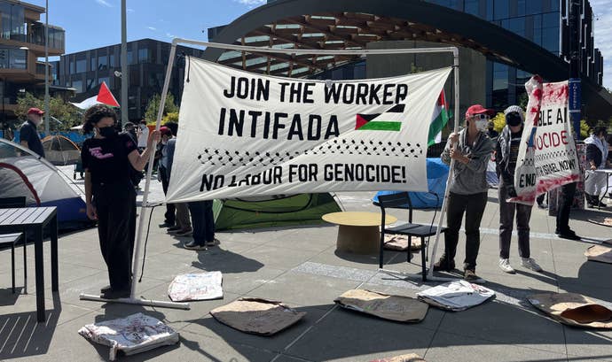 Protestors successful anti-viral masks holding a motion that reads "Join the idiosyncratic Intifada" and "No labour for genocide" astatine Microsoft's HQ during an concern to telephone for an extremity to Microsoft's concern narration with the Israeli military.