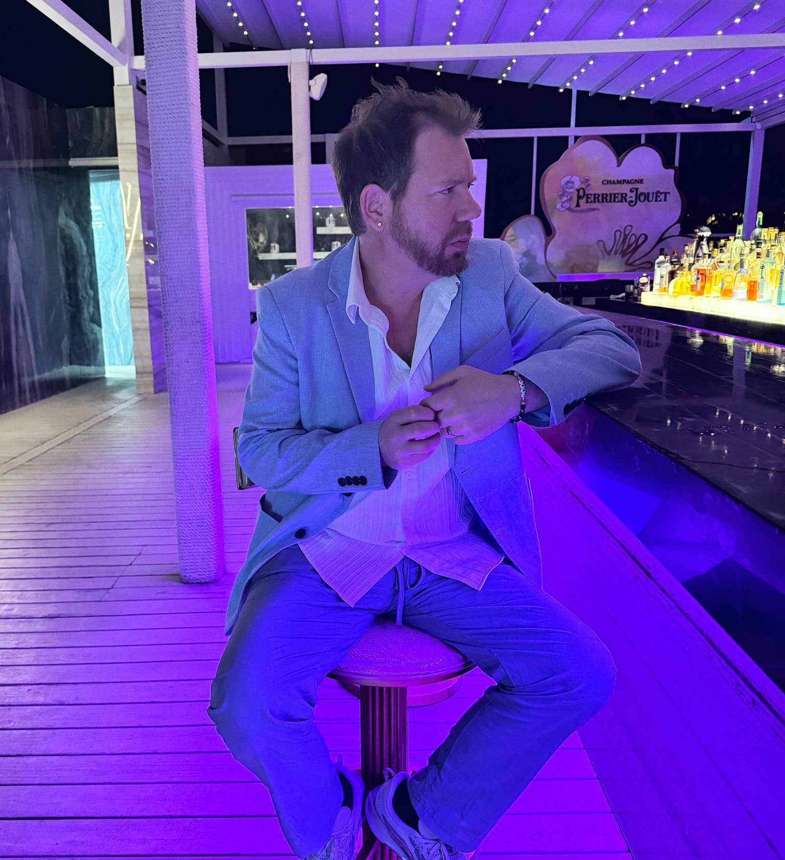 Image of Cliffy B sitting on a bar stool. He is wearing a light blue suit and a white shirt. He is looking to one side. Image from his social media