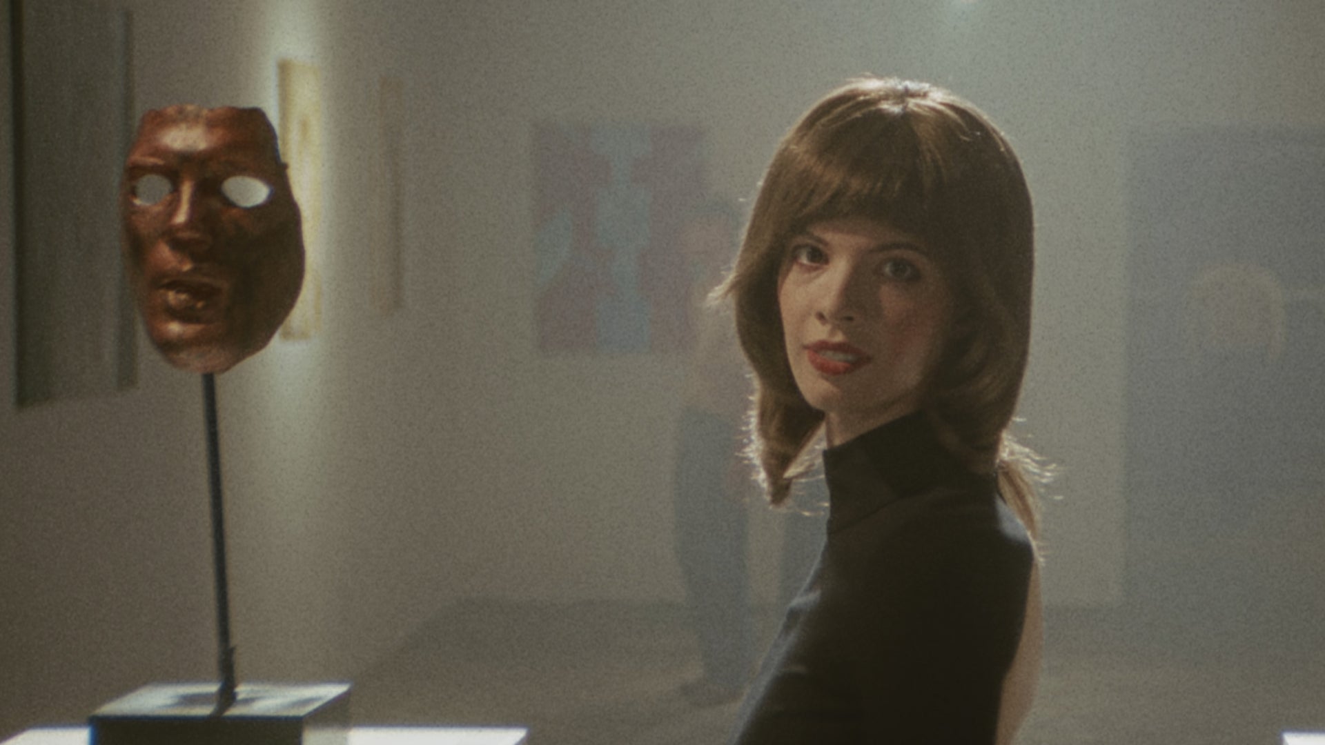 The character of Franny in Immortality&rsquo;s second Marissa Marcel film, Minsky, stands beside a mask at an art exhibition