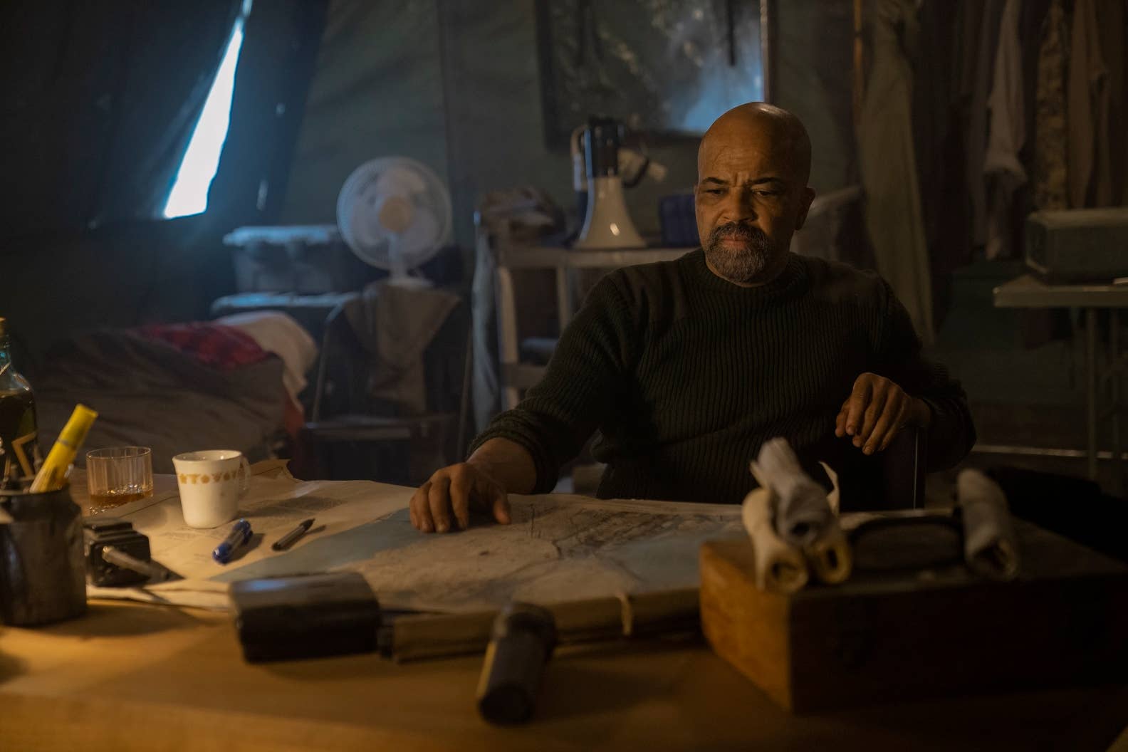 Isaac sits at a table which has a map and other stationery on it in TLOU season two