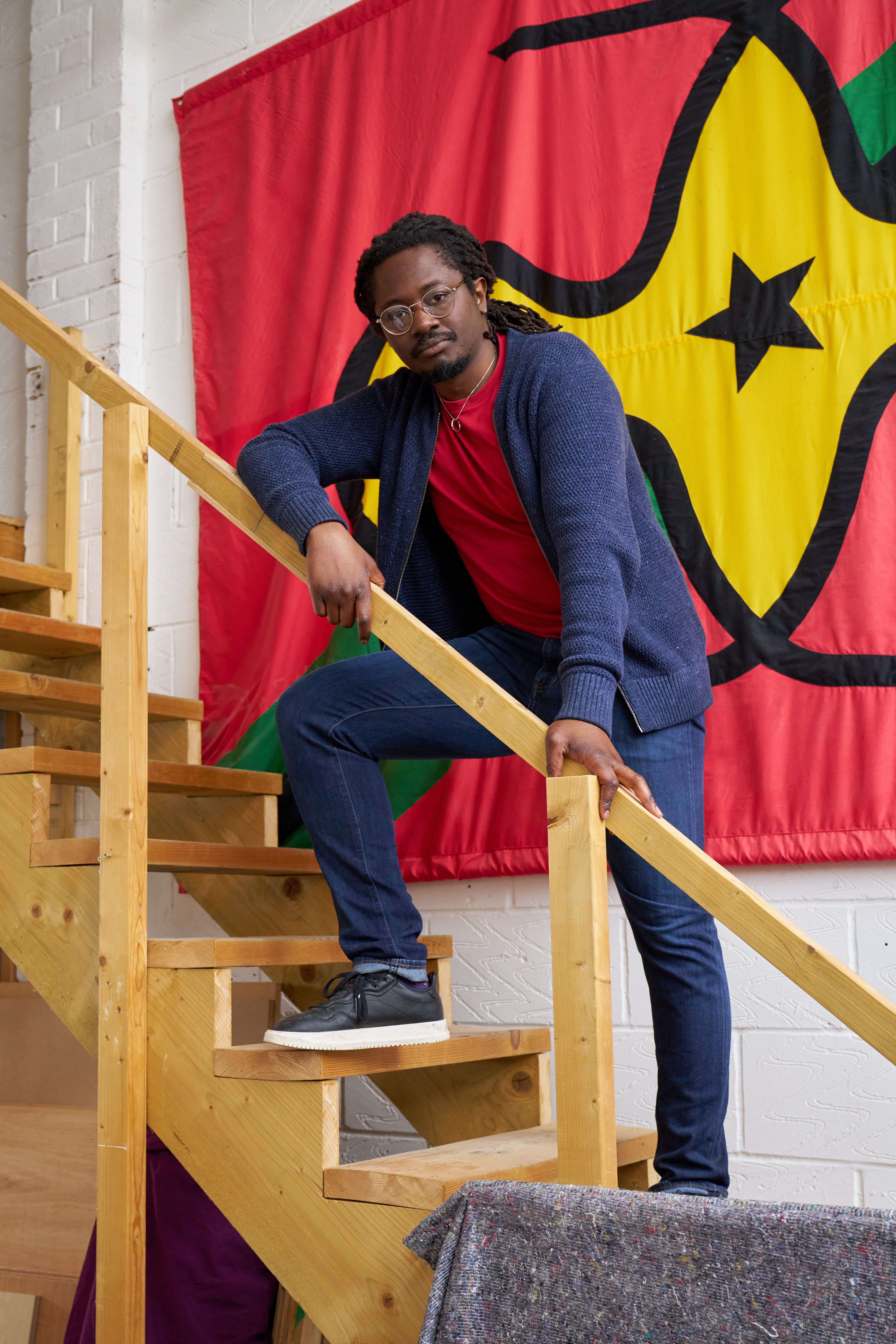 Larry Achiampong stands on steps in front of a piece of his art.