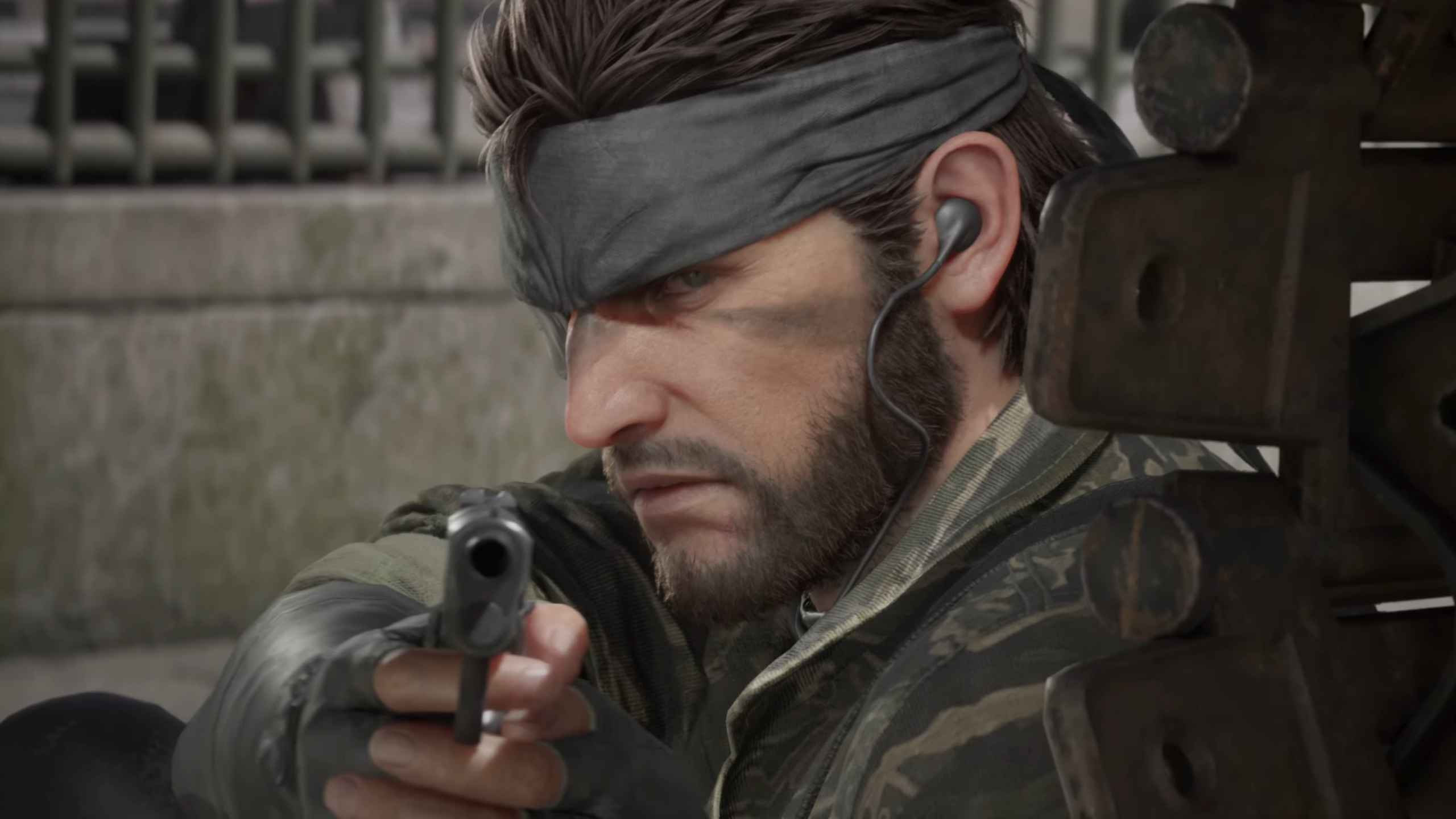 Metal Gear Solid Delta Snake Eater trailer screenshot showing close up of Snake with bandana aiming a pistol from behind cover