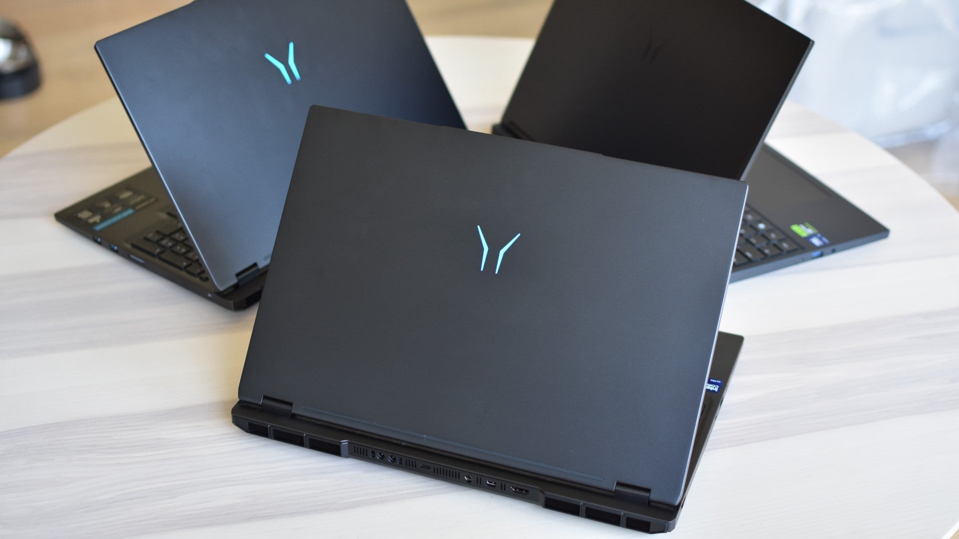 Three Medion Erazer gaming laptops on a table, open but with their lids facing the camera. - 3