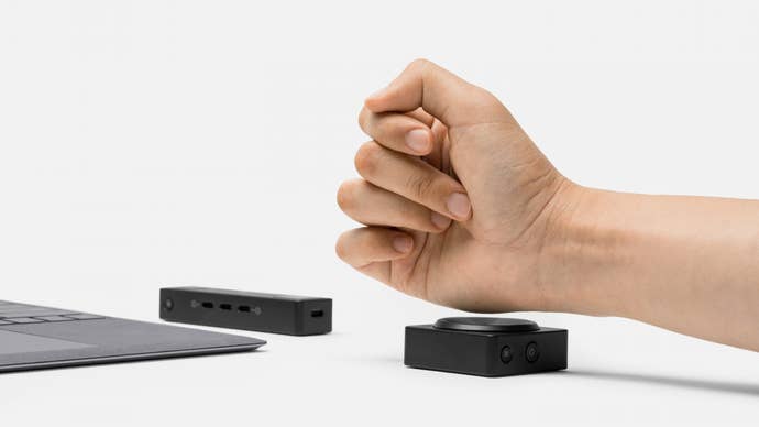 A clenched fist pressing down on a Microsoft Adaptive Button, with a Microsoft Adaptive Hub in the background.