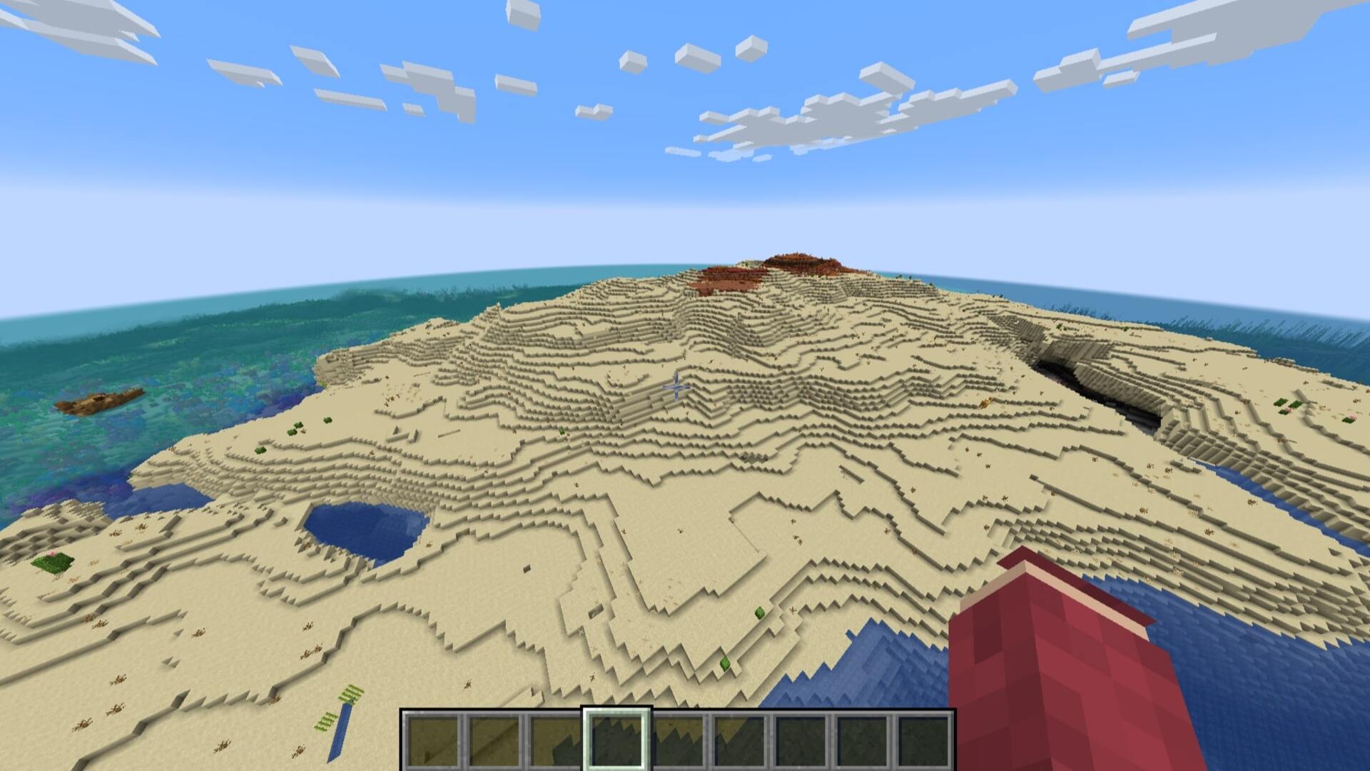 The player looks down at a large desert island with a nearby shipwreck in Minecraft