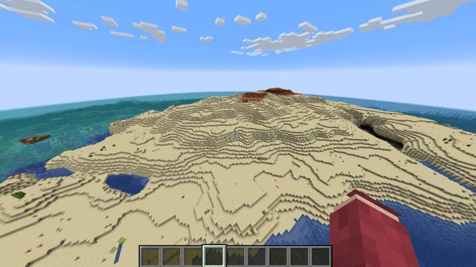 The player looks down at a large desert island with a nearby shipwreck in Minecraft