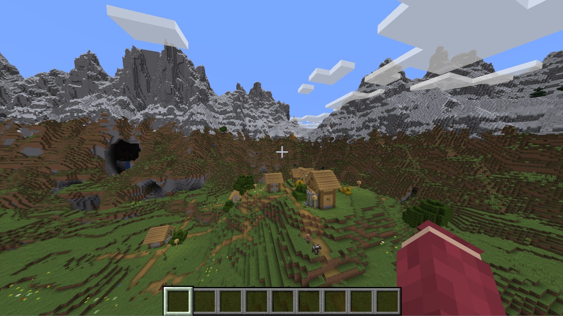 The player looks over at a small village surrounded by huge mountains in Minecraft