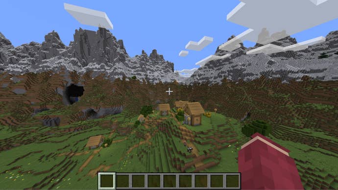 The player looks over at a small village surrounded by huge mountains in Minecraft