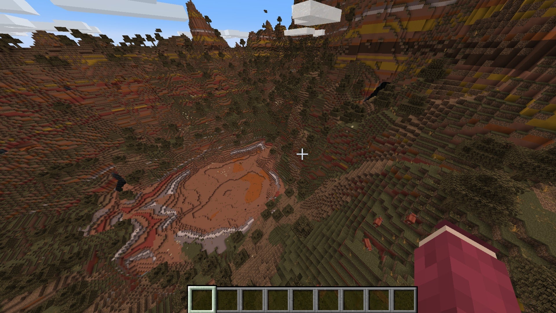The player looks down at a patch of flat land in the middle of a very mountainous badlands biome in Minecraft
