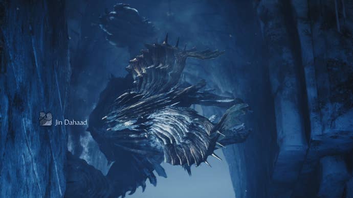 A Monster Hunter Wilds screenshot showing a giant monster Jin Dahaad climbing sideways along a wall toward the camera.