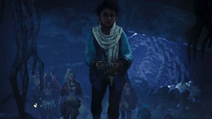 Monster Hunter Wilds screenshot showing a close-up of a child holding a glove in an underground cave with three people in the background.