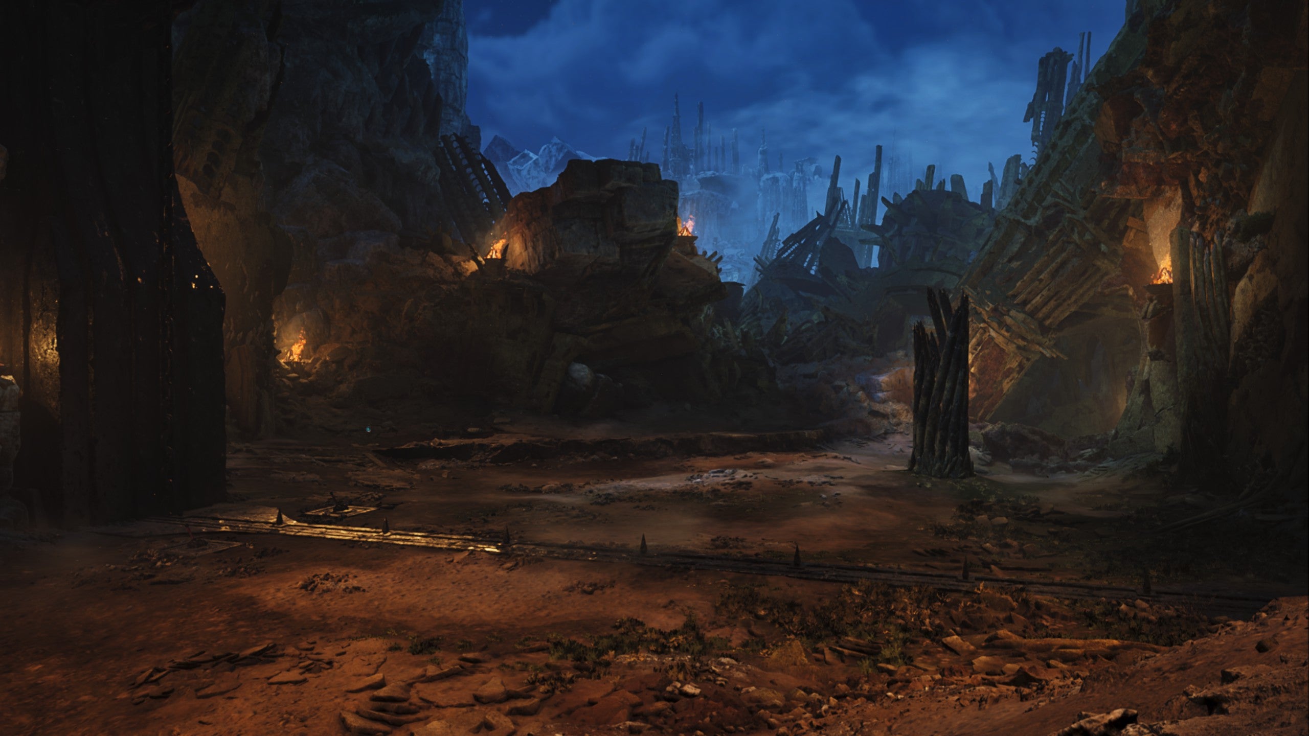 A Monster Hunter Wilds screenshot showing the Wounded Hollow monster arena at night lit up by torches and surrounded by rubble.
