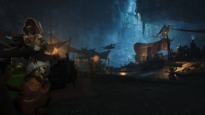 A Monster Hunter Wilds screenshot of the Scarlet Forest Base Camp inside a cave with light peeking through from above.