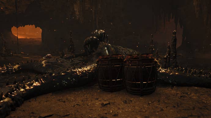 A Monster Hunter Wilds screenshot showing the Nu Udra monster sleeping inside a cave with two explosive barrels near them.