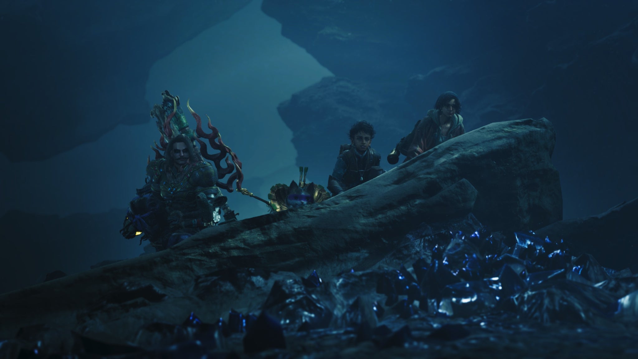 Dark Monster Hunter Wilds screenshot of three people and a palico ducking behind a rock with blue crystal fragments littered along the ground in front of it. - 9