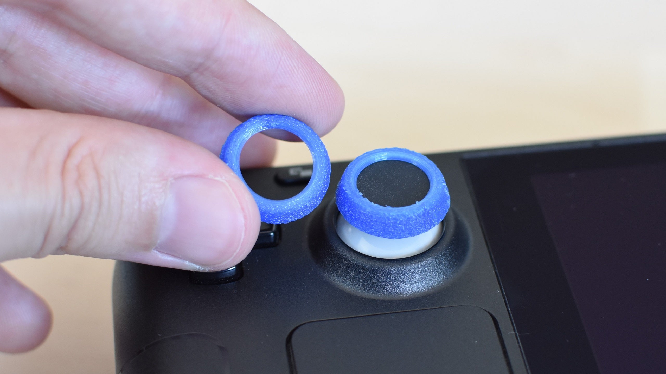 The NinjaPrint3D Steam Deck Thumb Grips. One is applied to the Steam Deck&rsquo;s left thumbstick, the other is being held next to it.