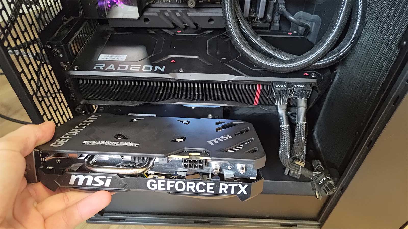 A RTX 4060 Ti graphics card being held next to an AMD Radeon 7900 XTX, the latter of which is installed in a PC.