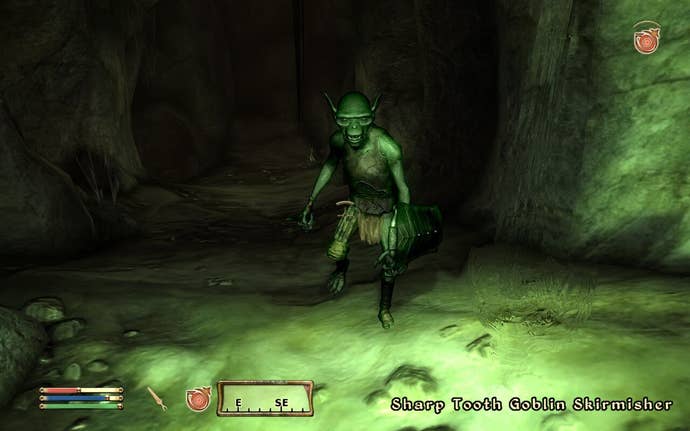 A goblin stands in the green light basement, enough in inactive pose, but has a shield.