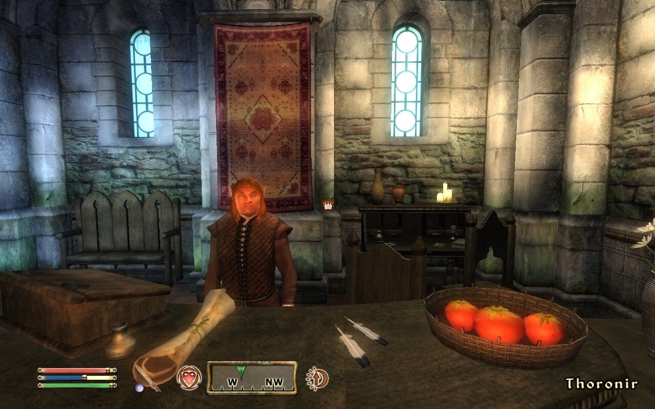 A man who looks too short is stood behind a table with what seems to be overly sized tomatoes on it.