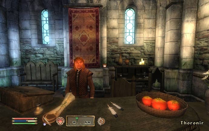 A man who looks too short is stood behind a table with what seems to be overly sized tomatoes on it.