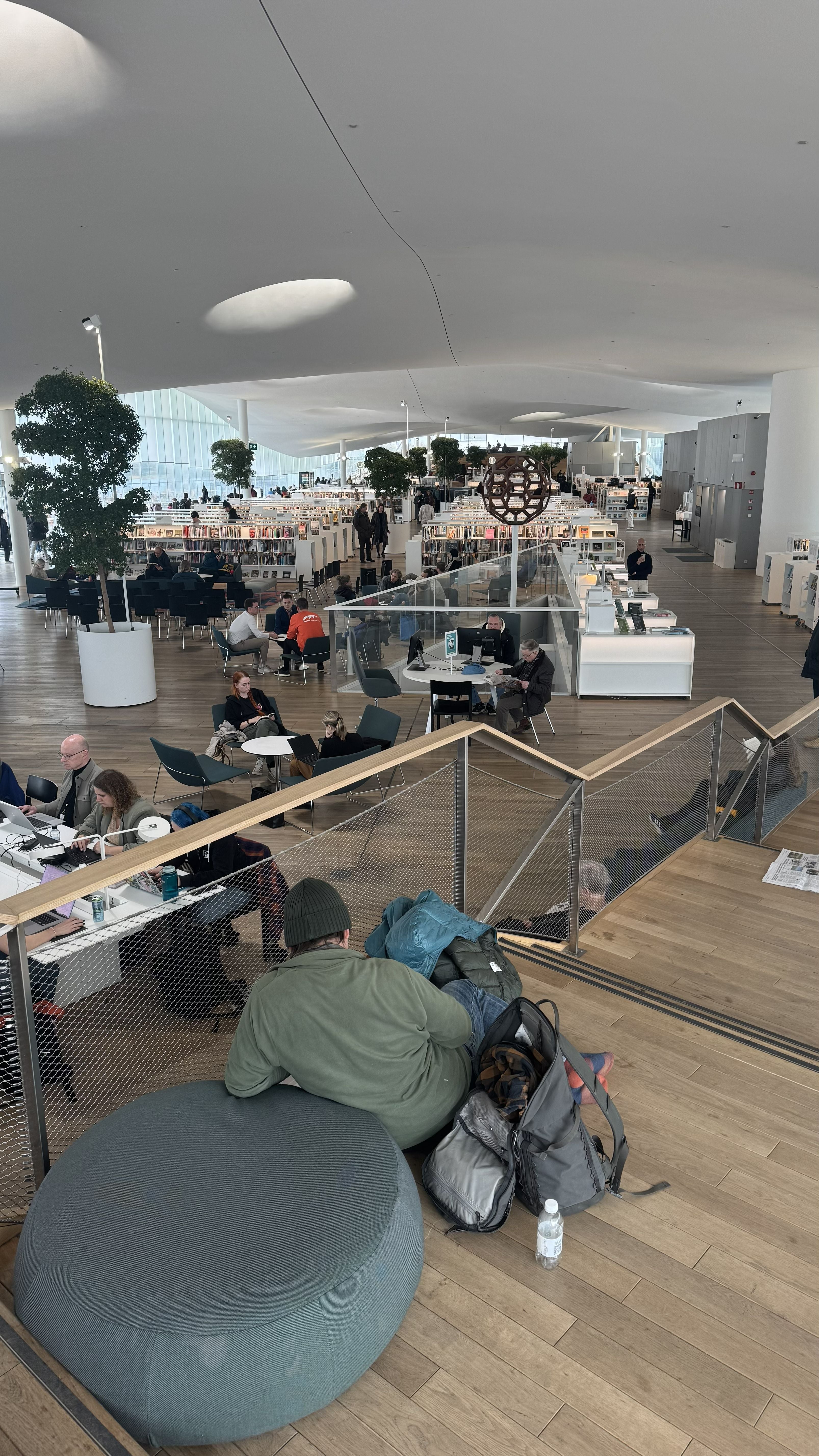 Photo of the Oodi Library in Helsinki showing a person reclining on a cushion, on a raised level looking over the top floor
