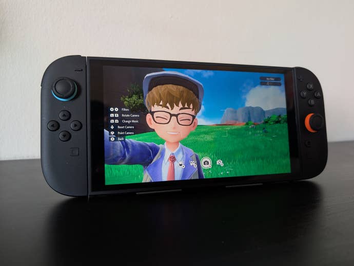 Trainer takes a selfie in Pokemon Scarlet and Violet, running on a Switch 2 on a black table against a white wall.